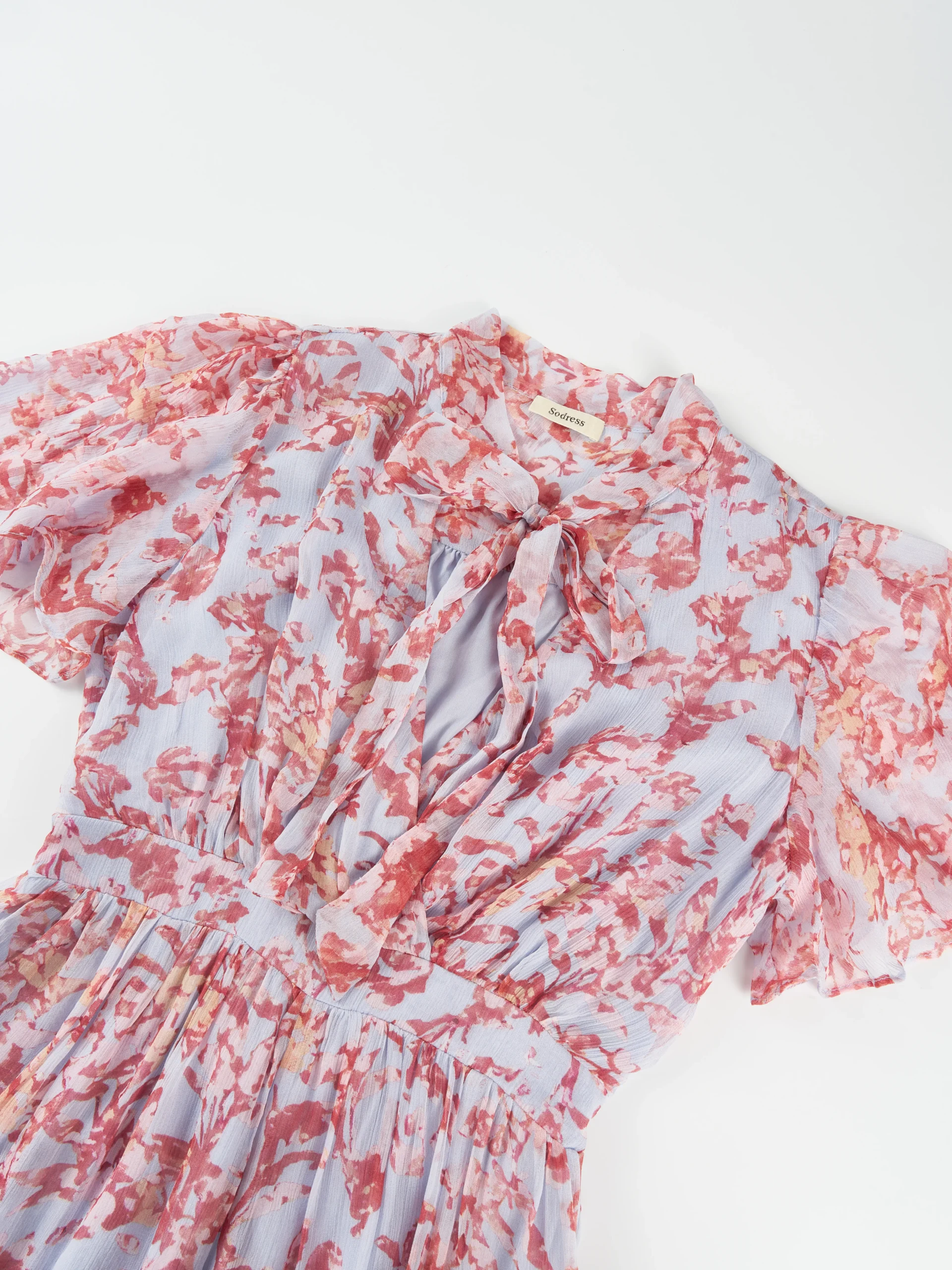 A lightweight floral mini dress featuring a feminine tie neckline, flutter sleeves, and a softly gathered waist. Its airy silhouette makes it ideal for summer collections, resort wear, and effortless everyday styling.