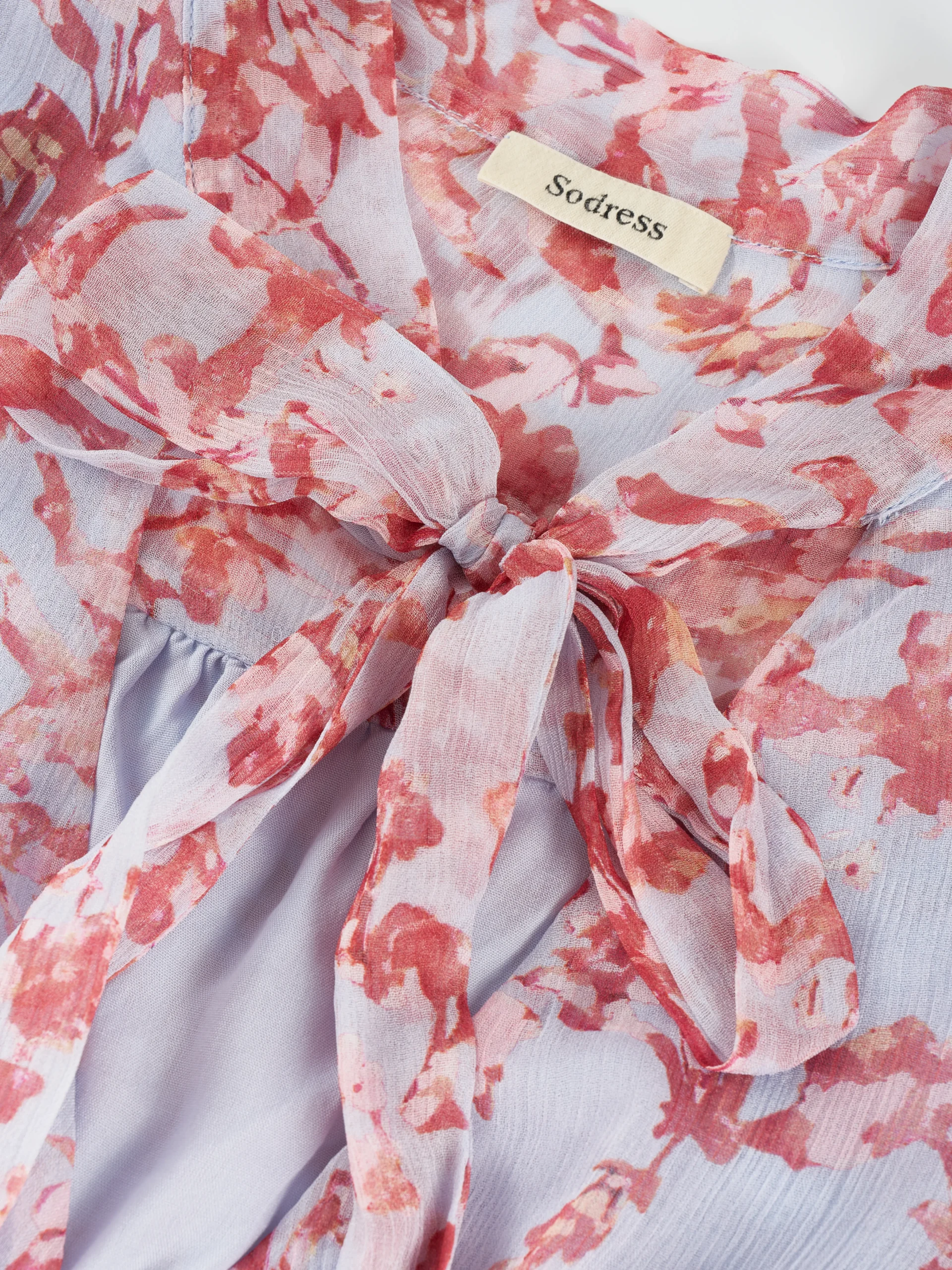 A lightweight floral mini dress featuring a feminine tie neckline, flutter sleeves, and a softly gathered waist. Its airy silhouette makes it ideal for summer collections, resort wear, and effortless everyday styling.