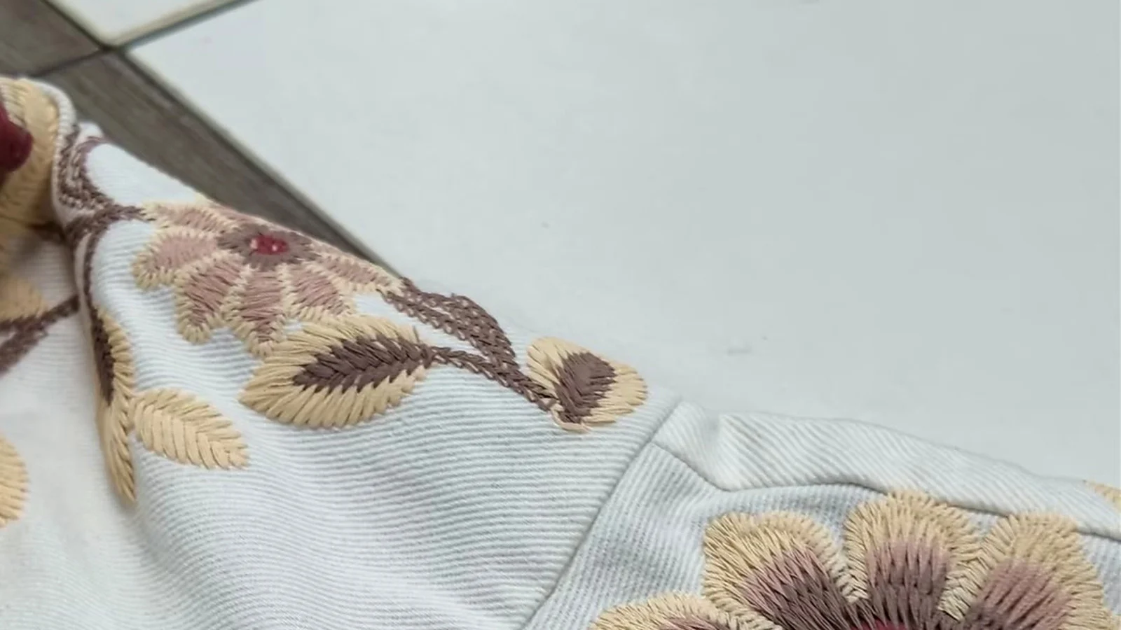 Beige floral embroidery placement around a garment shoulder seam