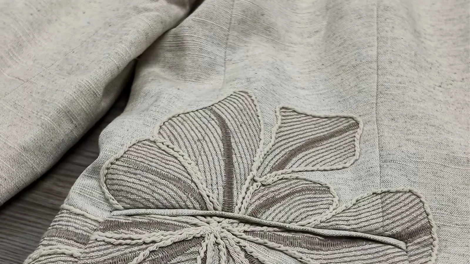 Close-up of dimensional floral embroidery on beige garment fabric