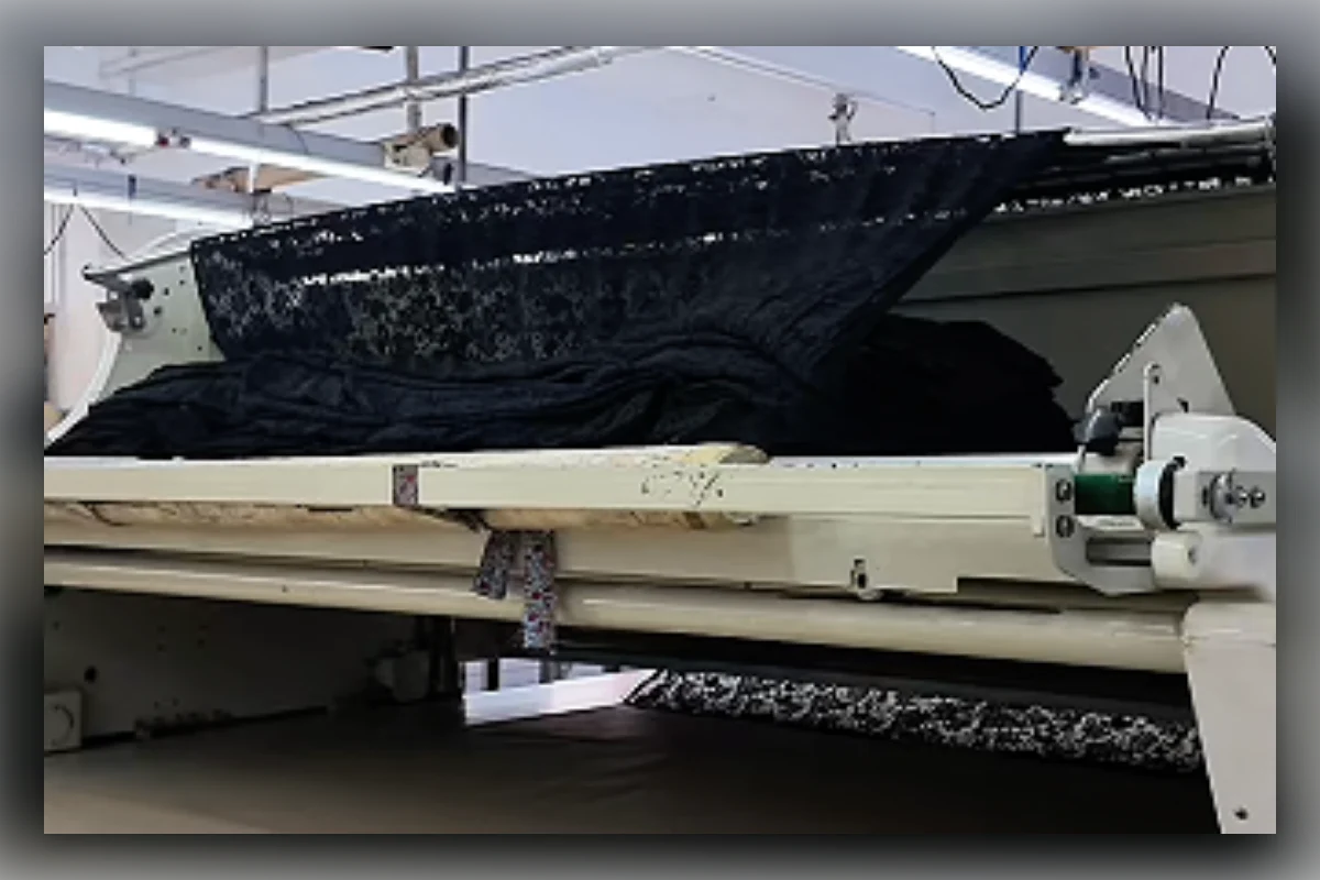 Automated fabric cutting machine processing layered black fabric