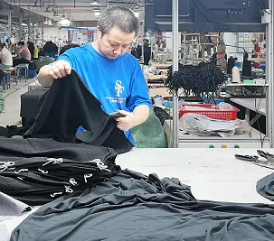 Worker inspecting a dark garment on a production table