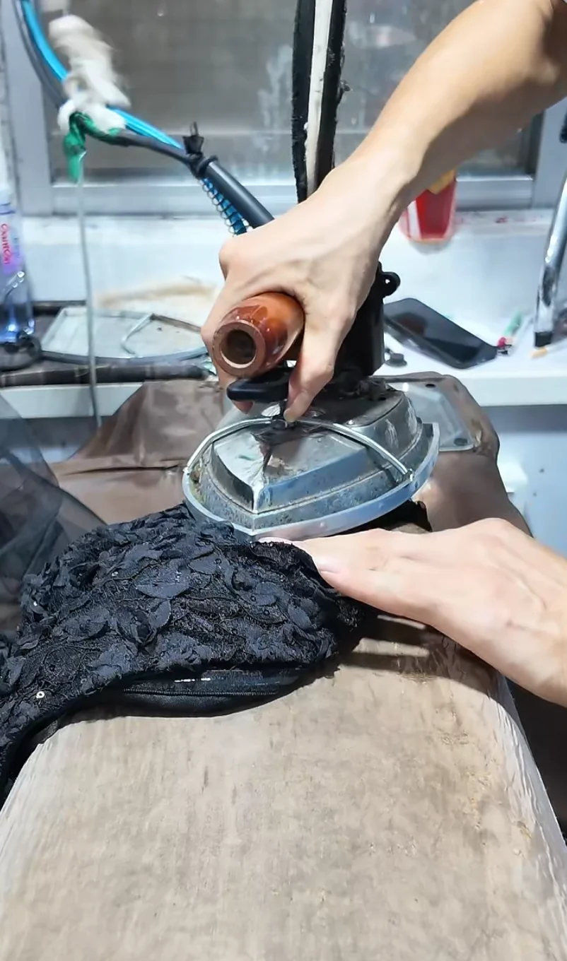 Worker pressing a dark garment on a padded station