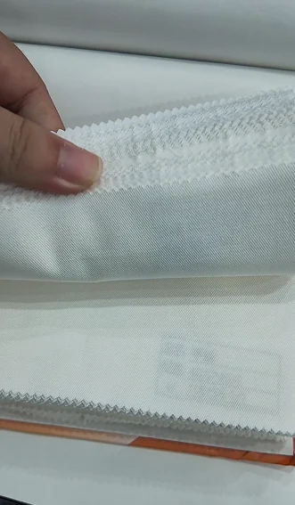 Hand lifting pale fabric to show its fall