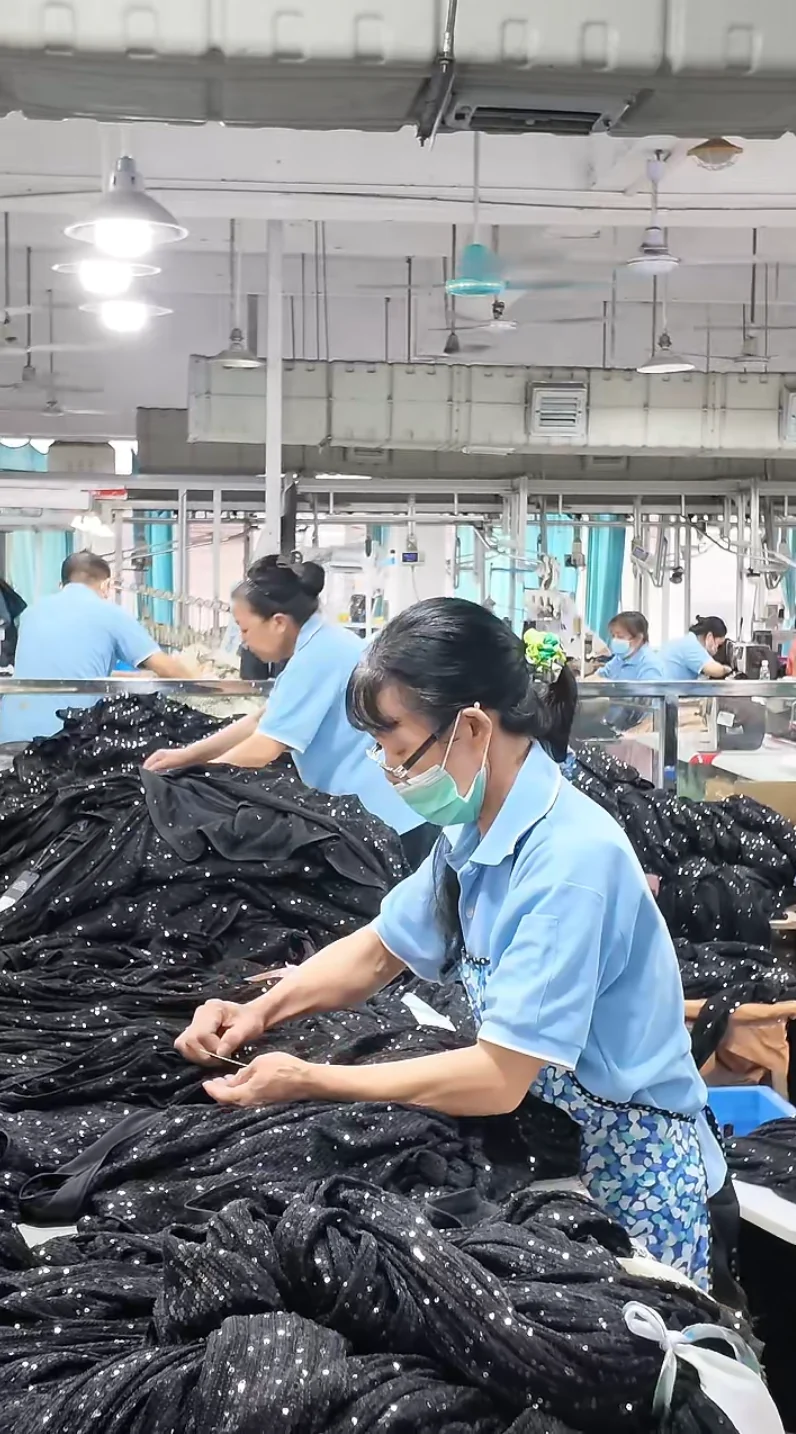 Workers handling dark garments at a finishing table