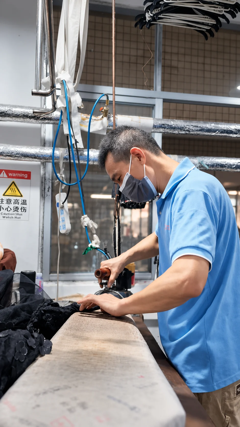 Worker handling a dark garment at a finishing table