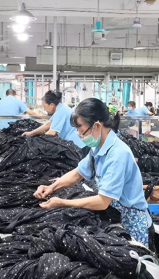Workers arranging dark garments at a production table