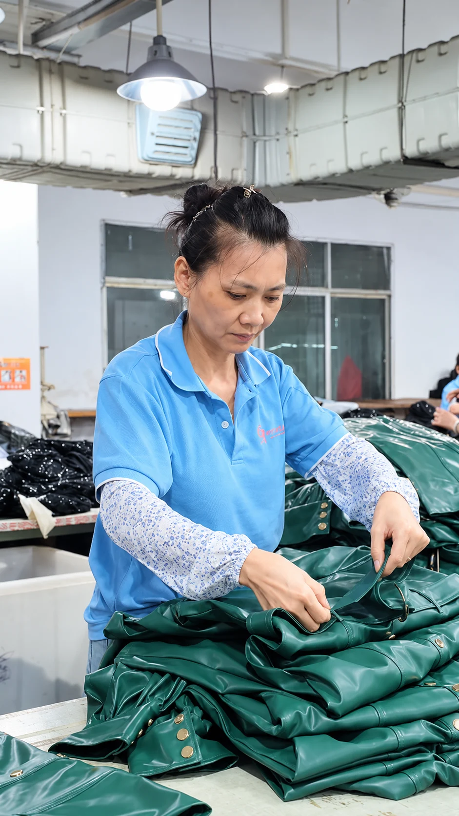 Worker handling green garments beside a sewing workstation