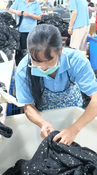 Worker handling a dark garment on a finishing table