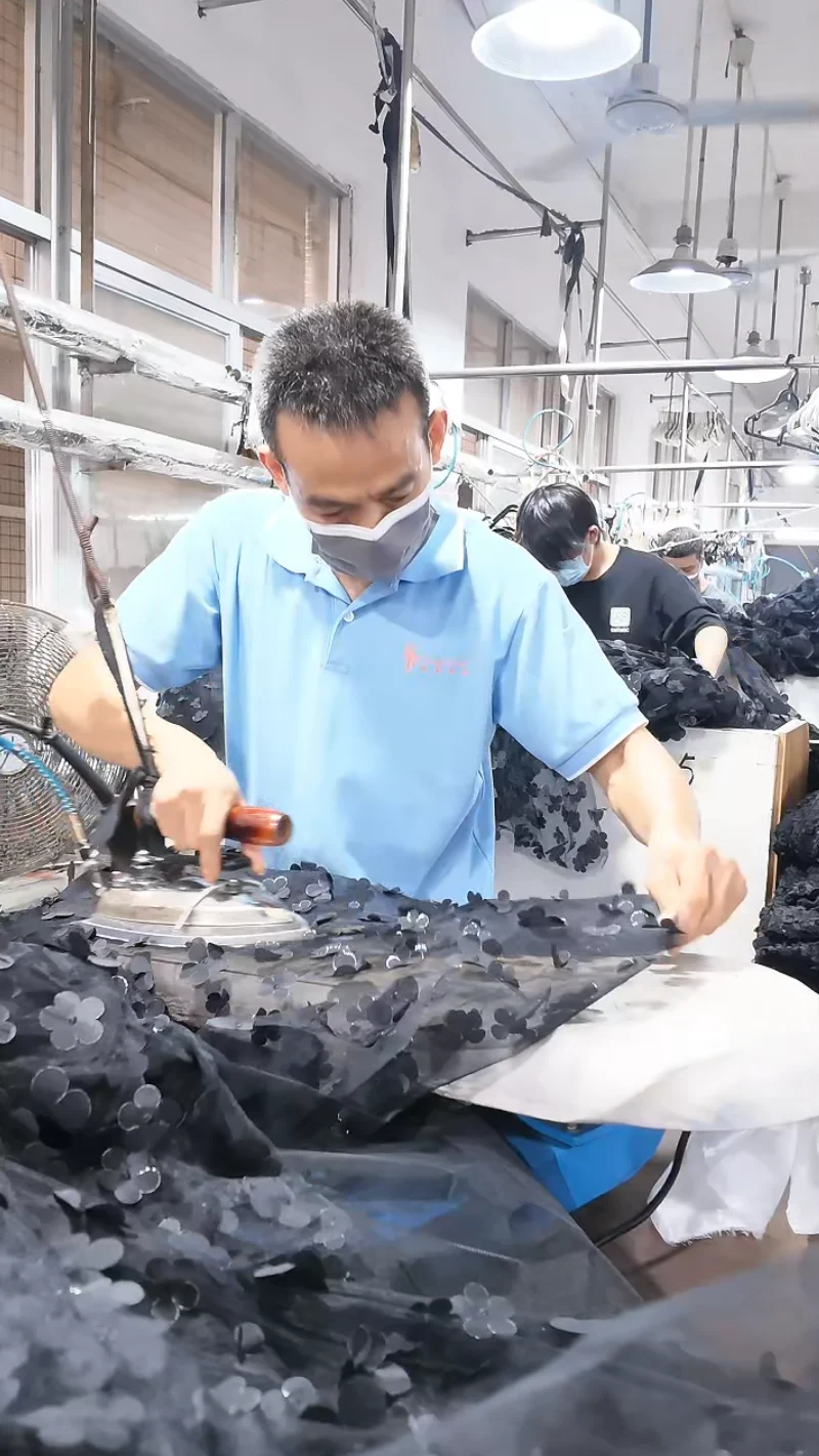 Worker handling a dark garment at a production station