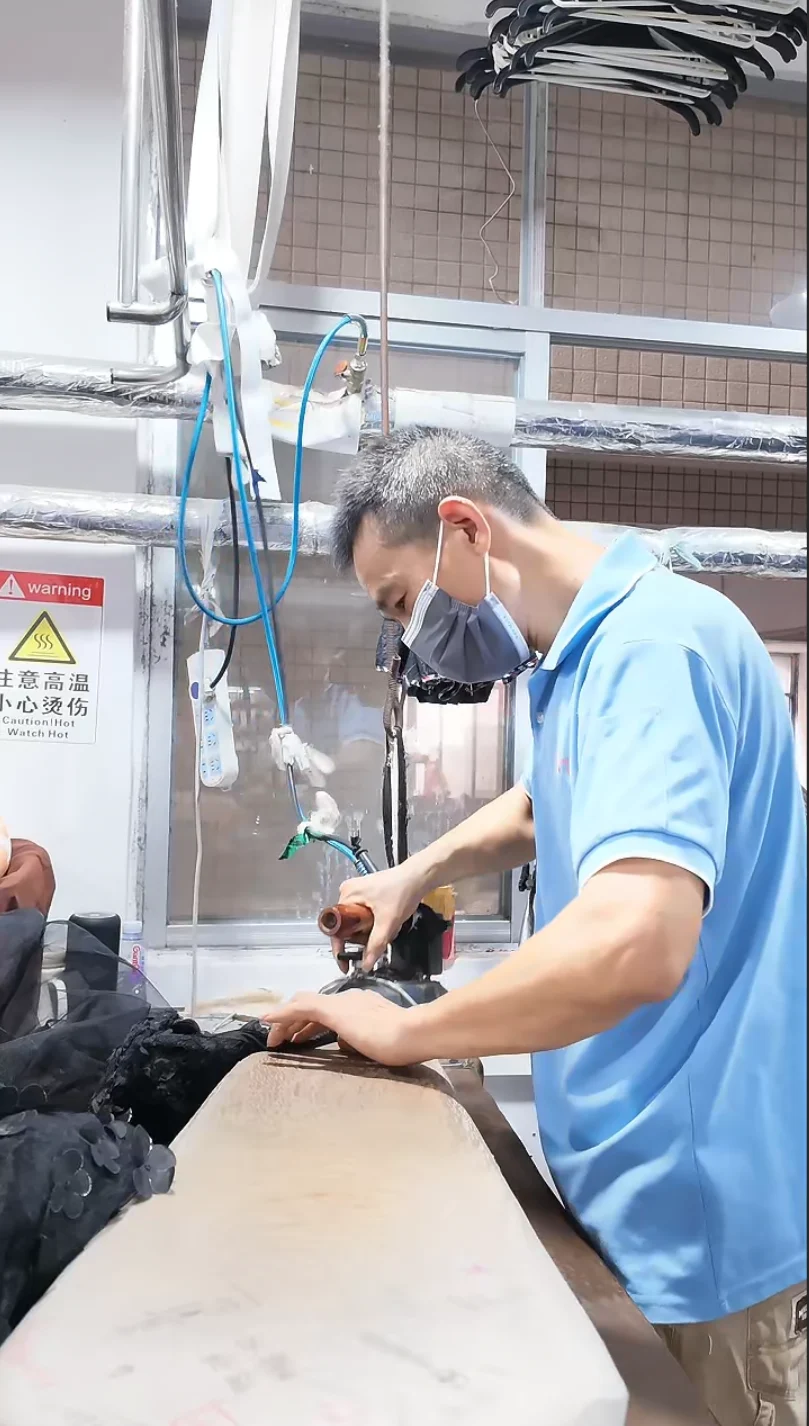 Worker handling a dark garment beside a pressing table