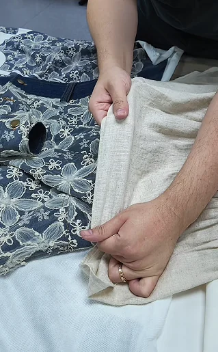 Hands comparing pale lining fabric with embroidered outer fabric